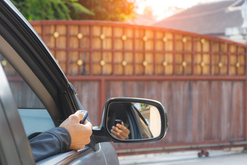Young man in car, hand using remote control to open the automatic gate while phoning and leaving...