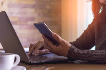 Casual woman or freelancer using mobile smart phone and working on laptop computer with cup of coffee on the table. Online working concept.