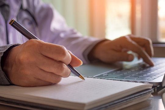 Female doctor work on laptop computer and write note at office in clinic.
