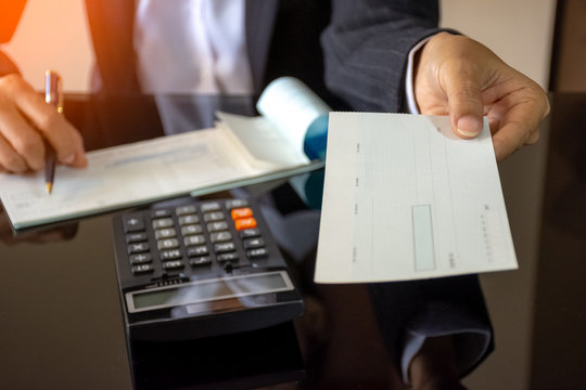 Businesswoman hand writing and giving cheque with calculator on the office desk . paycheck concept.	