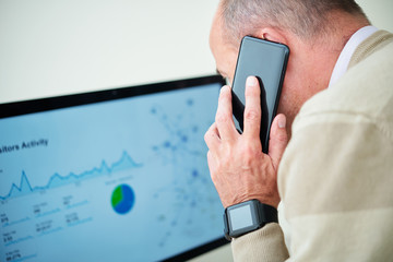 Businessman talking on phone with coworker when checking chart of visitors activity on computer screen