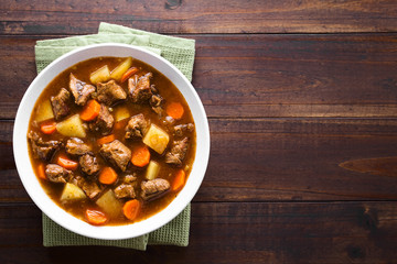 Fresh homemade beef stew with carrot and potatoes served in bowl, photographed overhead with copy space on the side