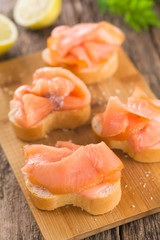 Smoked salmon slices on baguette on wooden board (Selective Focus, Focus on the first salmon slice)