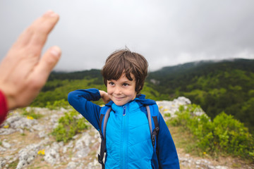 A boy with a backpack climbed to the top of the mountain and gives five.