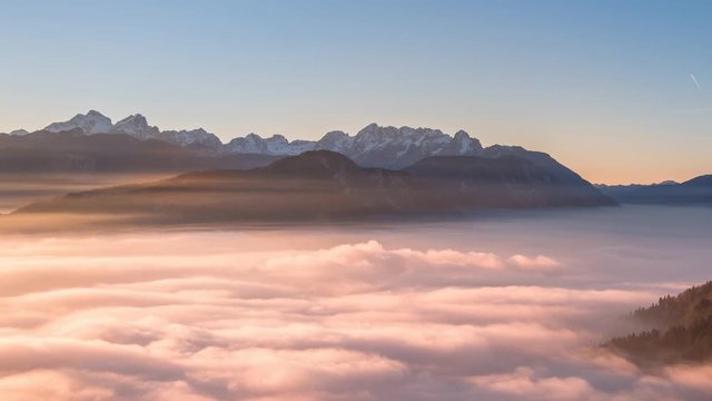Vivid time-lapse of rolling fog and clouds at sunset below the mighty mountain landscape.