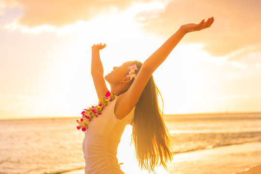 Hawaii hula dancer woman wearing flower necklace lei on sunset beach dancing with open arms free in sunset relaxing on hawaiian travel vacation. Asian girl with fresh flowers hair, traditional dance.