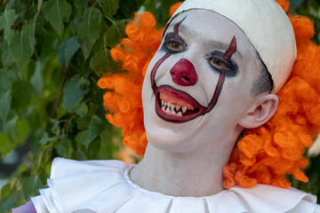 A street performer in a costume of an evil clown similar to Pennywise on a background of green...
