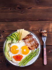 Top vertical view of ketogenic diet breakfast on the white plate with a fork on dark wooden background with copy space