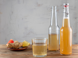 Two bottles and glass of kombucha drink on a wooden table with a ginger and a slice of grapefruit on the plate. With copy space