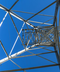 Fototapeta premium Supports high-voltage power lines against the blue sky. View from the bottom up