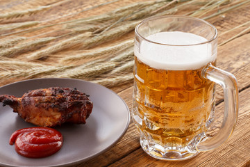 Glass of beer, plate with grilled chicken and ears of barley on a wooden background.