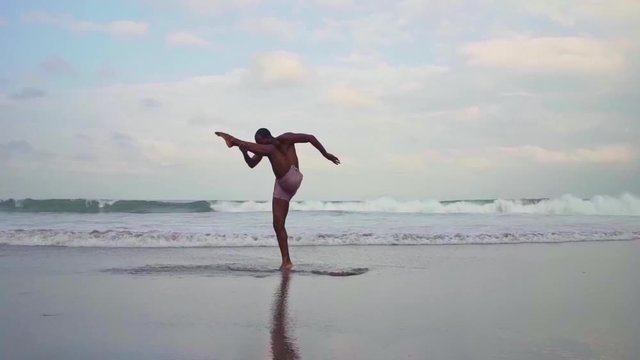 Contemporary ballet dancer performing at the beach. Gimbal shot on young attractive and athletic black African American man dancing by the sea