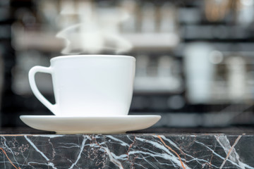 Steaming coffee cup with smoke on marble table in coffee shop
