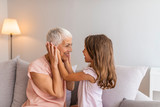 Granddaughter embracing her grandmother in living room. Her granddaughter holds the key to her heart. Grandmother and granddaughter. Smiling senior woman and girl embracing