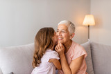 Happy middle-aged mature grandma and little preschool granddaughter touching noses laughing together, smiling loving old grandmother granny and cute carefree grandkid girl having fun playing at home