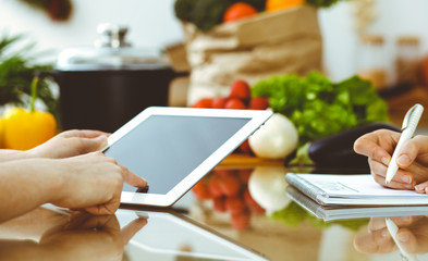 Close-up of human hands using tablet or touch pad. Two women in kitchen. Cooking, friendship or family fun concepts