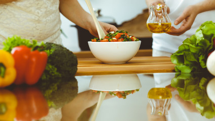 Closeup of human hands cooking in kitchen. Mother and daughter or two female friends cutting vegetables for fresh salad. Friendship, family dinner and lifestyle concepts