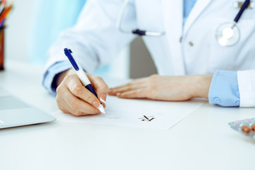 Female doctor filling up prescription form while sitting at the desk in hospital closeup. Healthcare, insurance and excellent service in medicine concept