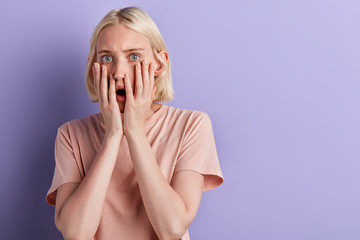 Young blonde shocked woman touching her cheeks with palms, being shocked with news, big sale, discounts, close up portrait, copy space.facial expression