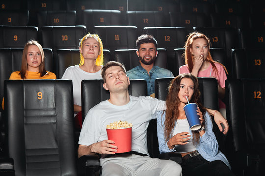young tired man sleeping at the cinema, while other people looking at the screen. close up photo