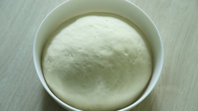 Dough rising, time lapse. Yeast dough rising on white bowl on wooden table. Pizza dough, khachapuri dough