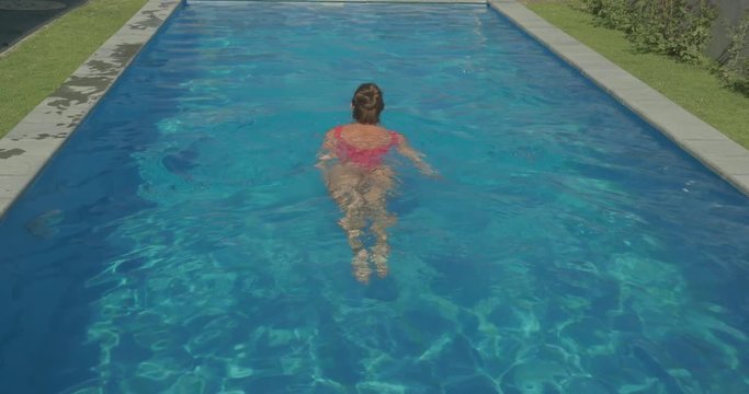 Back view of beautiful woman in red swimsuit swimming in the outdoor pool - video in slow motion