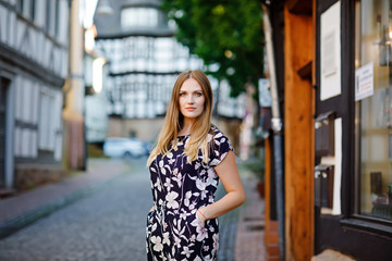 Beautiful young woman with long hairs in summer dress going for a walk in German city. Happy girl enjoying walking in cute small fachwerk town with old houses in Germany.