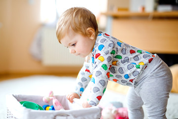 Gorgeous cute beautiful little baby girl playing with educational toys at home or nursery. Happy healthy child learning crawling and standing.