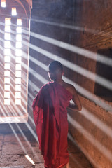 young buddhist novice monk dressed in red traditional robe praying in a buddhist temple wrapped in sunbeams