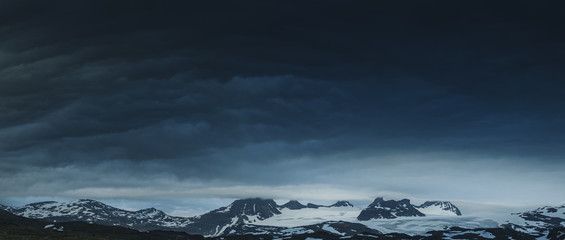 Fototapeta premium Panorama of gloomy cloudy Norwegeian mountains covered in snow, Norway