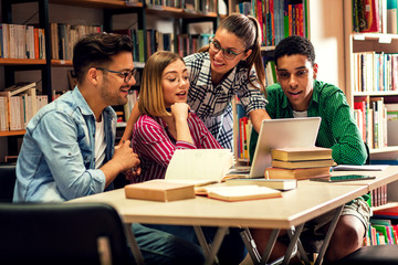 Four young students study in the school library, female student using laptop for researching online.