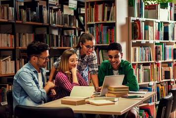 Four young students study in the school library, female student using laptop for researching online.