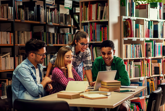 Four young students study in the school library, female student using laptop for researching online.