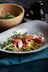 Salad with crab and avocado on a dark background. Arugula salad leaves seasoned with sauce on white wine with crab meat and grilled avocado in soft focus. Top view