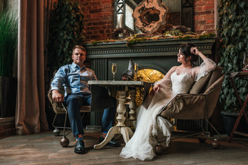 Beautiful wedding couple posing on camera in a restaurant. Newlyweds sit by the fireplace and hold hands, the concept is a new family, a beautiful wedding.