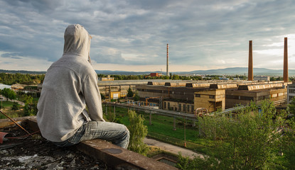 Fototapeta premium Young man in hood sitting and enjoy view to city Ceske Budejovice in sunset with old foundry, Czech republic