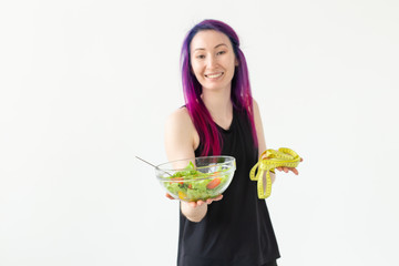 Young fitness blogger girl holding vegetable salad and measuring tape. Concept of sports lifestyle and proper nutrition. White background with copy space