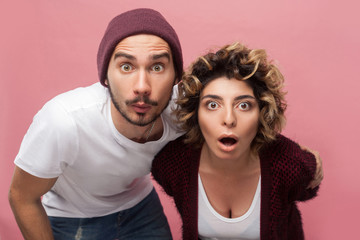 Closeup portrait of shocked funny couple of friends in casual style standing with unbeliveable face and looking at camera with big eyes and opened mouth. Isolated,indoor, studio shot, pink background - obrazy, fototapety, plakaty