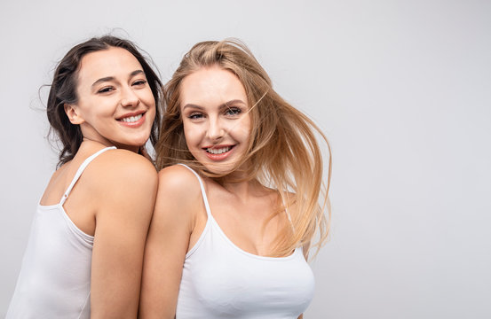 Smiling girls in white tank tops nestling each other looking at camera isolated white background copyspace