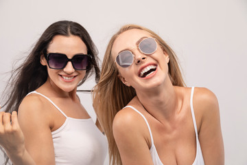 Beautiful blonde and brunette models in tank tops and sunglasses laughing isolated white background