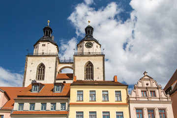 Fototapeta na wymiar Lutherstadt Wittenberg, Details der Häuser am Kirchplatz sowie die Türme der Stadtkirche Wittenbergs vor Wolken und Himmel