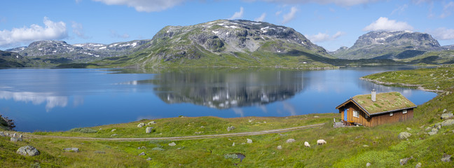 Peat roofed hut on Lake Stavatn with mountains reflected in it, Norway