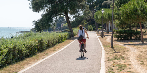 young woman on bike ride in summer day in La Rochelle city in France in web banner template