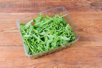 Fresh arugula leaves in container on rustic table, top view