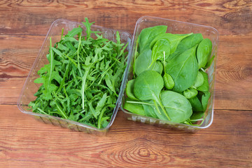 Fresh arugula and spinach leaves in containers on rustic table