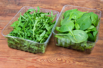Arugula and spinach leaves in two containers on rustic table