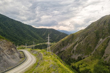 Asphalt road   with huge power transmission towers. Landscape with beautiful mountain road with a perfect asphalt. High rocks, amazing sky at sunset in summer.  Travel background. Highway at mountains