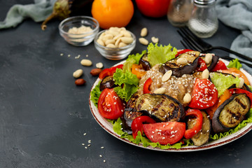 Salad with eggplant, tomato, paprika, lettuce, sesame and peanuts on a plate on dark background, horizontal orientation, copy space