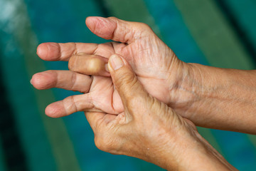 Trigger Finger, Senior woman's left hand massaging her middle finger, Suffering from pain, Close up and macro shot, Swimming pool background, Health care concept