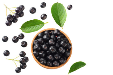 Chokeberry in wooden bowl with green leaves isolated on white background. Black aronia. Top view.